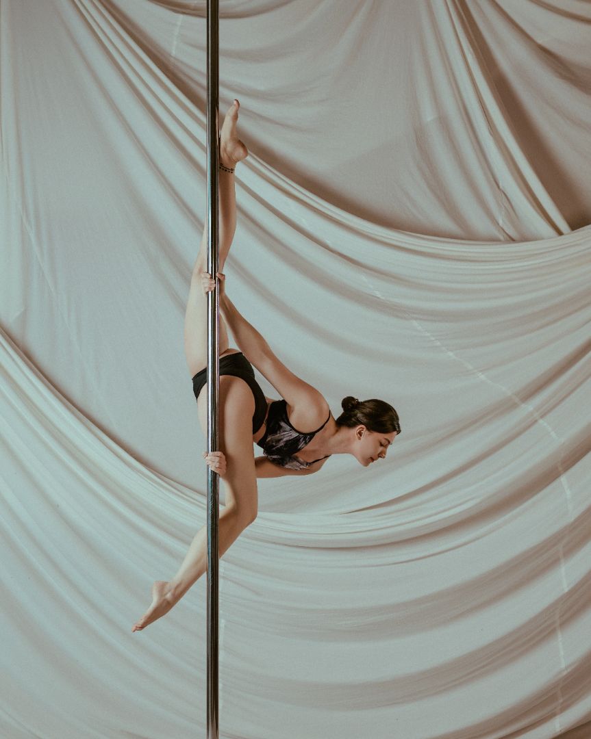 Pole dancer wearing the Nabi Polewear Signature Set performing a pole move against a draped fabric background