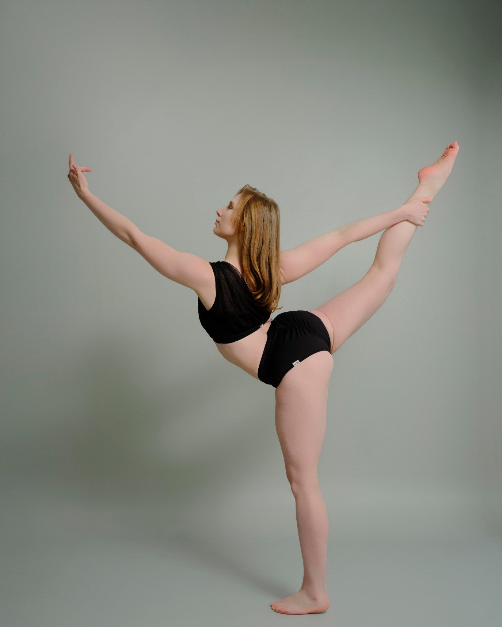 Woman performing a dance pose in the Metamorphosis Signature Set - Black, available in sizes S, M, L. Sustainable polewear designed for flexibility and elegance.

