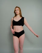 Woman wearing the Metamorphosis Signature Set - Black, featuring a mesh overlay and flattering V-cut bottom. Available in sizes S, M, L for a confident fit.