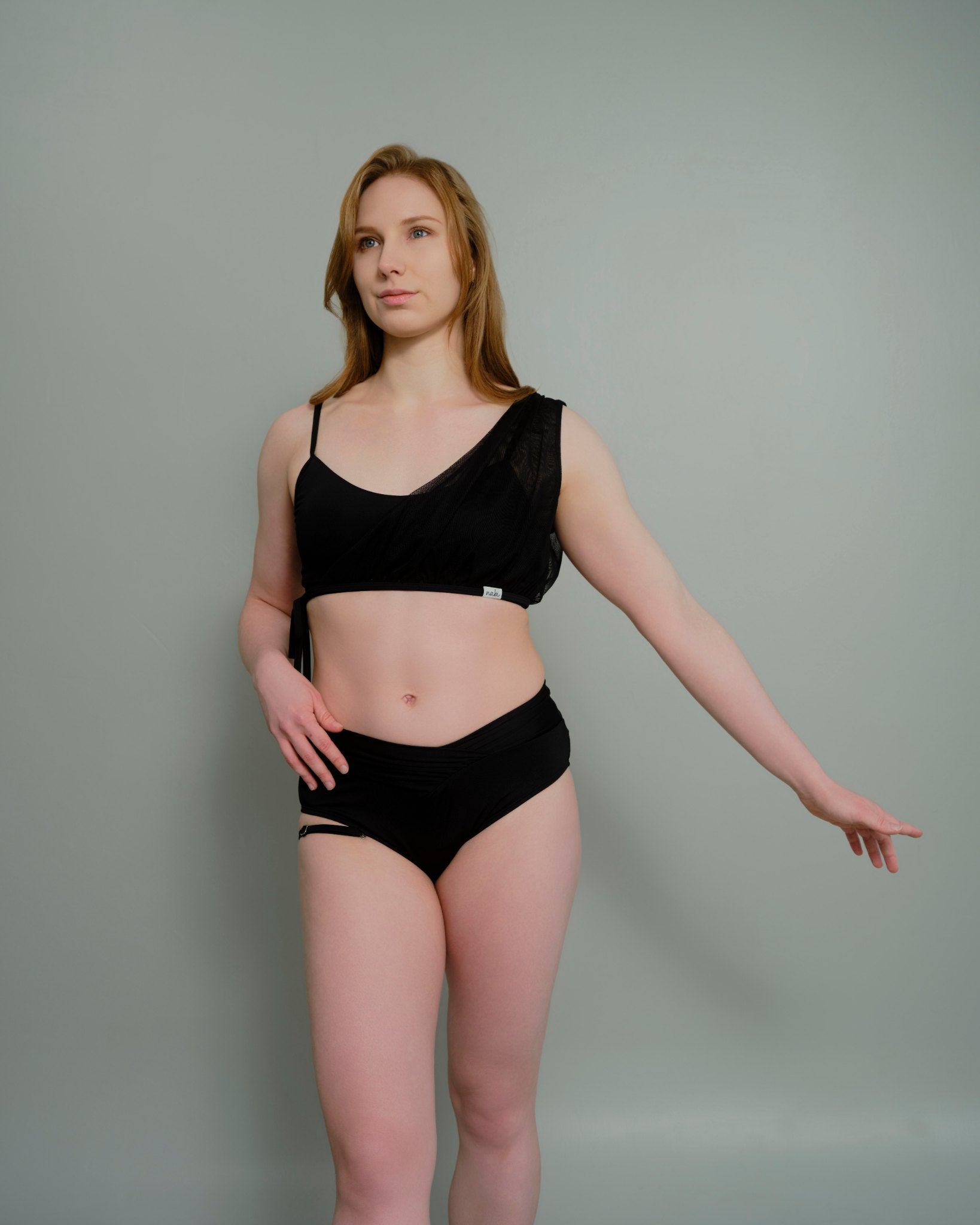 Woman wearing the Metamorphosis Signature Set - Black, featuring a mesh overlay and flattering V-cut bottom. Available in sizes S, M, L for a confident fit.