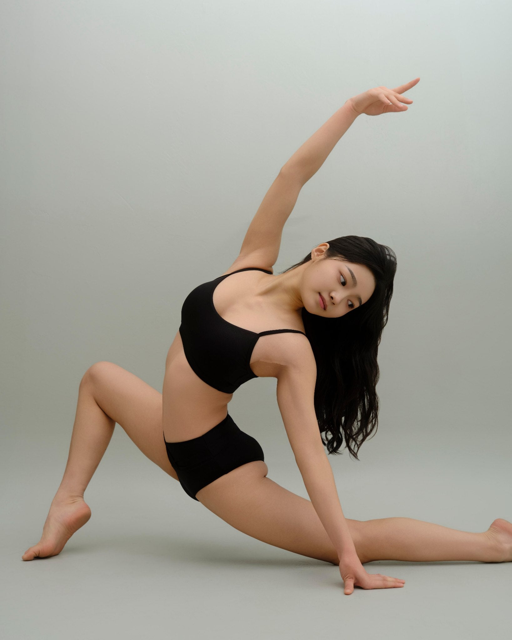 Woman stretching in the Metamorphosis Signature Set - Black, available in sizes S, M, L. Sustainable polewear designed for flexibility, comfort, and style.