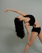 Woman performing a graceful pose in the Metamorphosis Signature Set - Black, available in sizes S, M, L. Sustainable polewear designed for comfort and movement.

