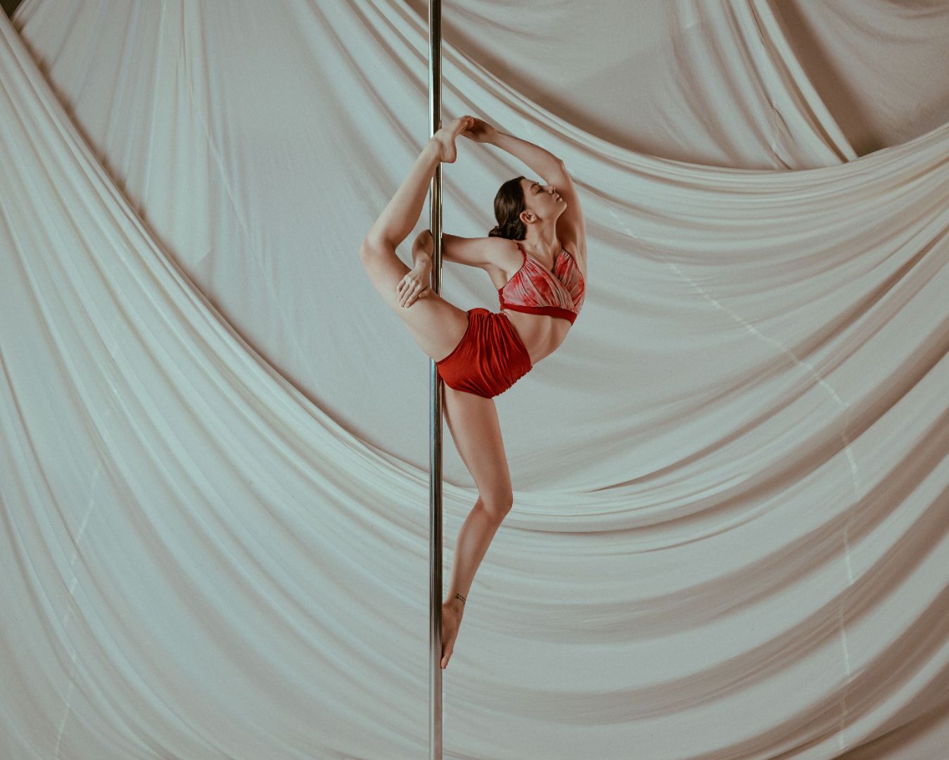 Person in red outfit pole dancing against a draped white curtain