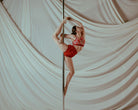 Person in red outfit pole dancing against a draped white curtain
