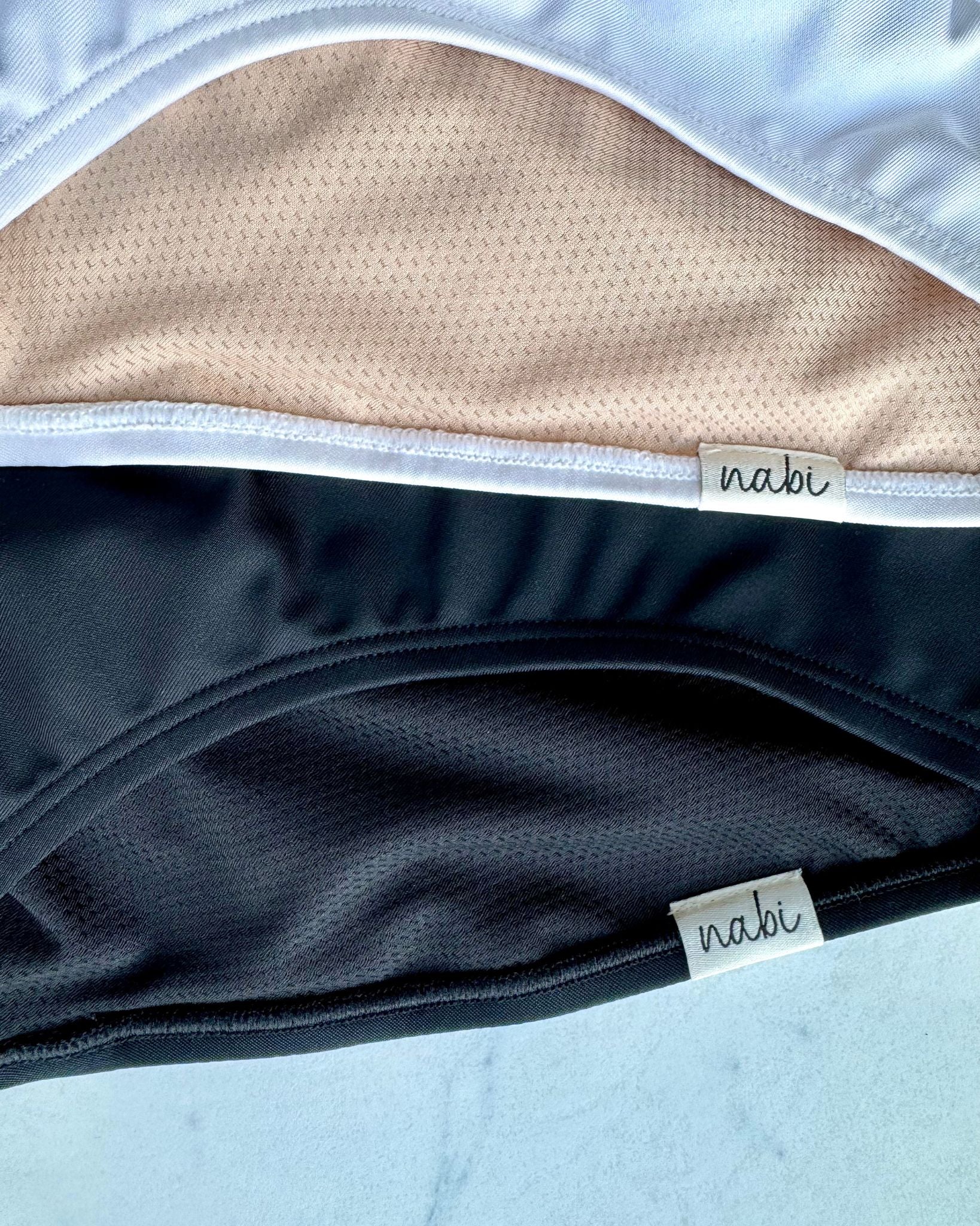 Close-up of Metamorphosis Signature Tops in White and Black, made from Regen® recycled polyester with soft mesh lining. Sustainable materials. Sizes S, M, L.
