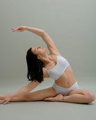 Woman stretching in Metamorphosis Signature Set - White, available in sizes S, M, L. Sustainable polewear designed for flexibility, comfort, and elegant movements.